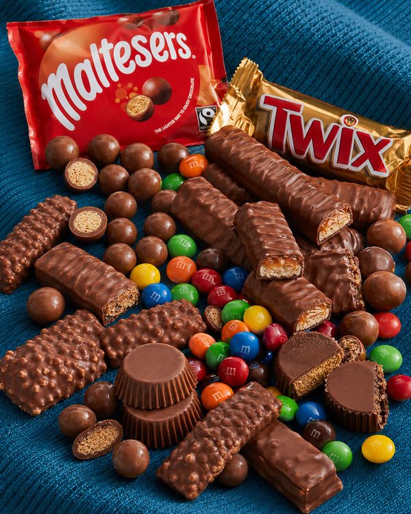 A pile of ordinary chocolate bars and candy-coated sweets on a blue background