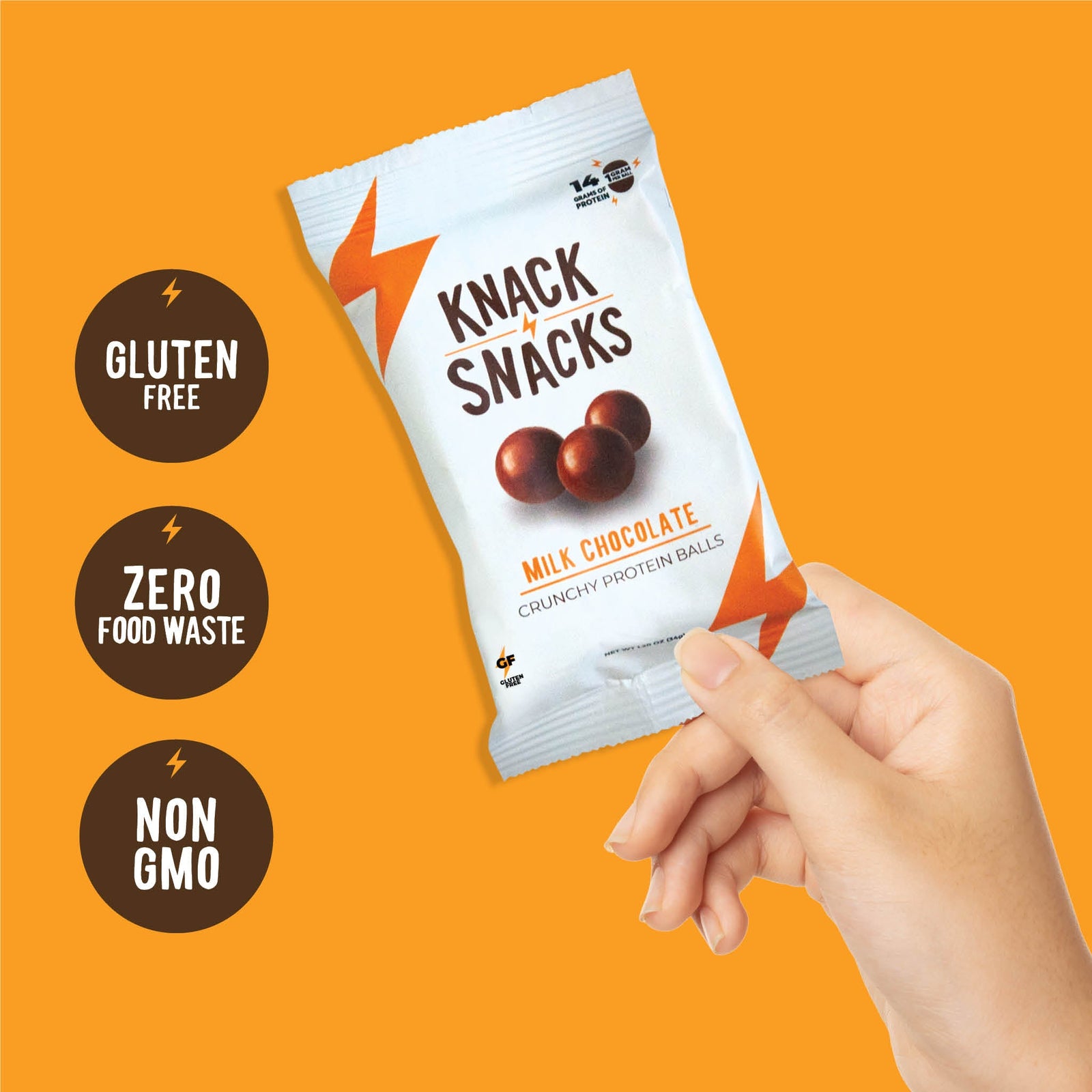 A hand holding a pack of Knack Snacks milk chocolate crunchy protein balls, next to gluten-free, zero food waste and non-GMO badges